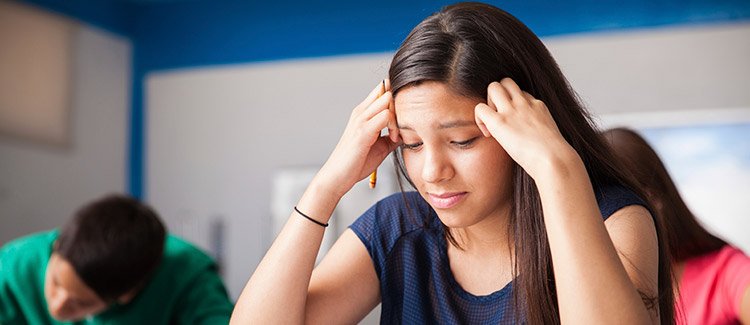 Photo of a young girl, possibly high school age, looking down at her test or homework and obviously stressed.