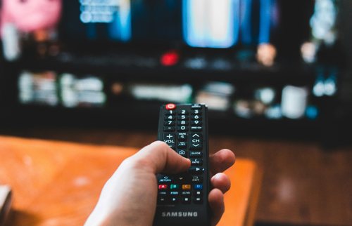 Photo of someone holding a remote and pointing it at a television. This photo is associated with an article on how to get your child away from the TV.